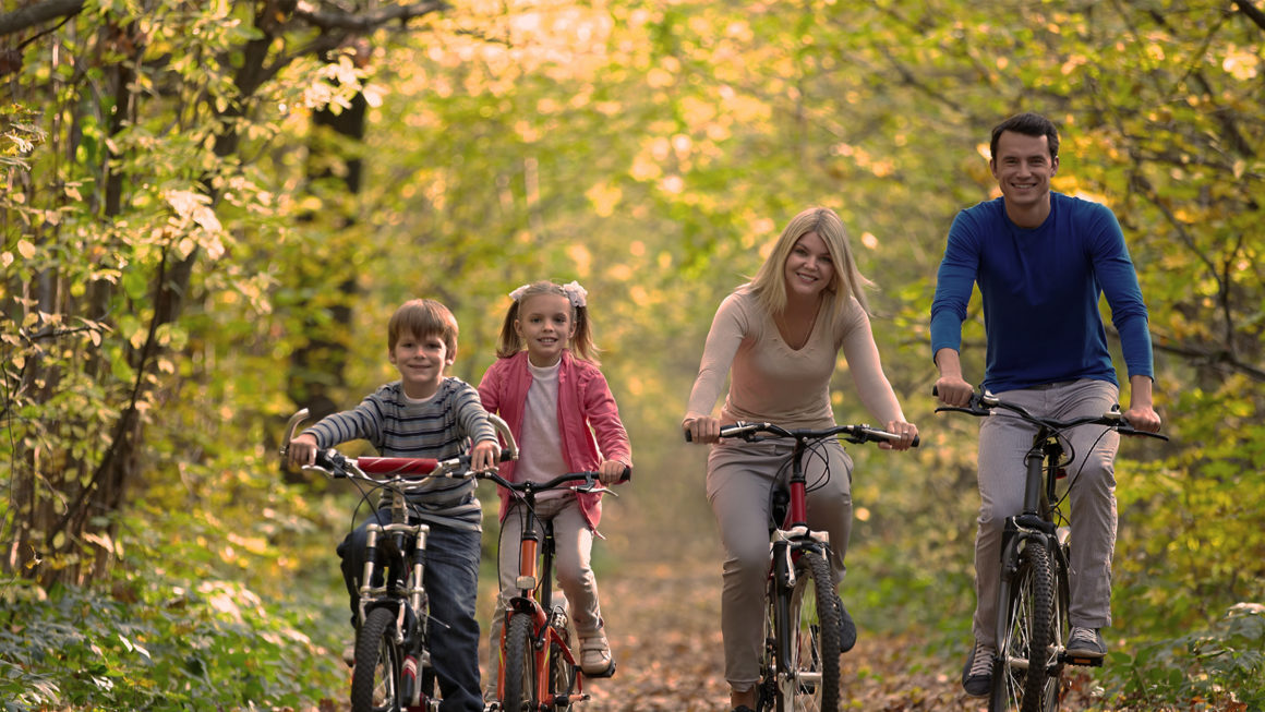 smiling family riding bikes in a park during autumn