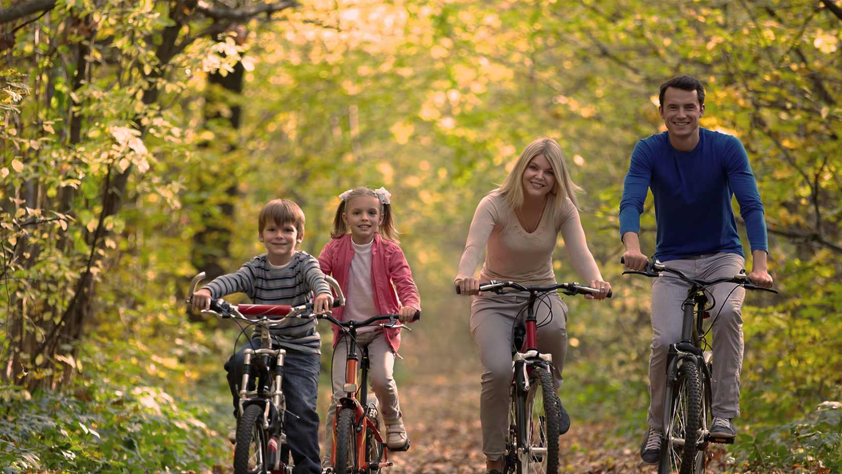 smiling family riding bikes in a park during autumn