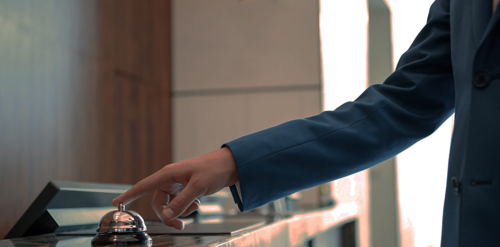 Closeup of a businessman hand ringing silver service bell on hotel reception desk