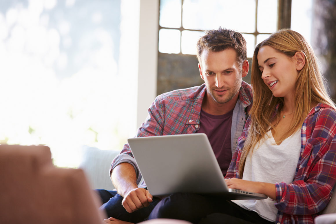 young couple in flannel shirts paying their bills online with a laptop