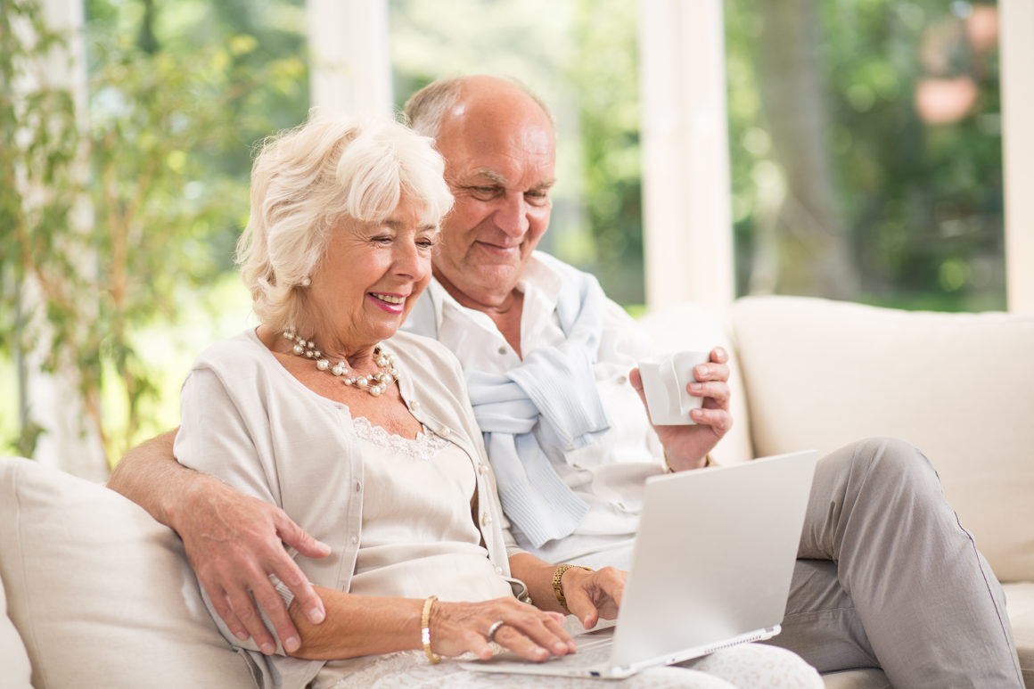 happy elderly couple using a laptop to pay their apartment rent online while drinking coffee