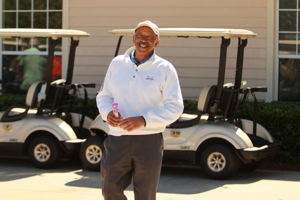 man smiling in golf attire in front of a golf cart