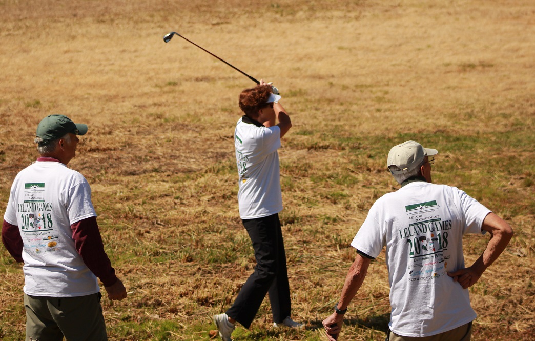 one woman playing golf with two men watching at leland games