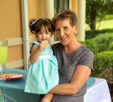 a grandmother happily holding her granddaughter, who is eating a cookie