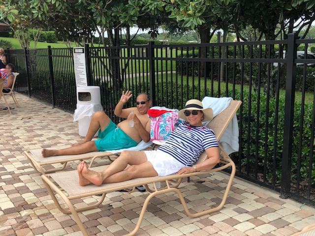 happy couple laying out by the pool and waving to the camera